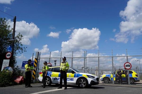 Police officers guard a fence, blocking off the access road to the Brook House immigration removal centre beside Gatwick Airport