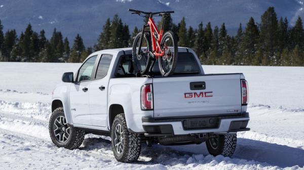 White GMC Canyon truck driving in snow, carrying a red mountain bike.