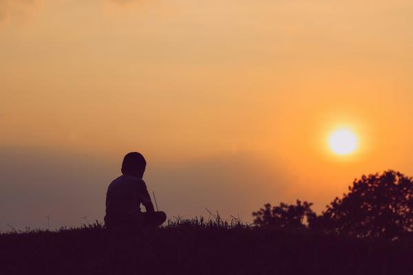 A little boy silhouetted against an orange sky as the sun sets.